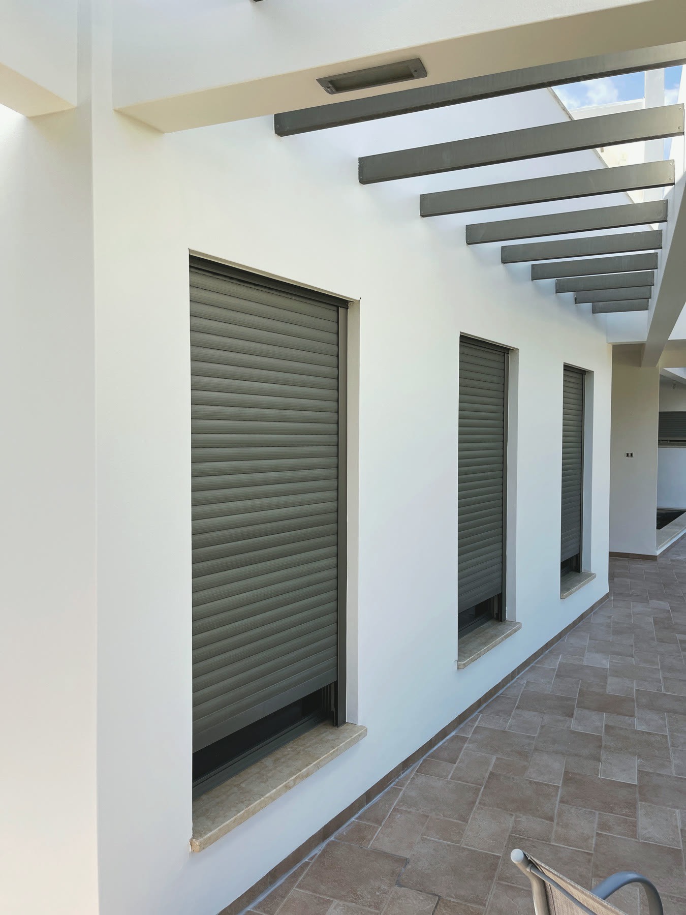 A white exterior corridor with grey pergola beams and shutters, freshly painted