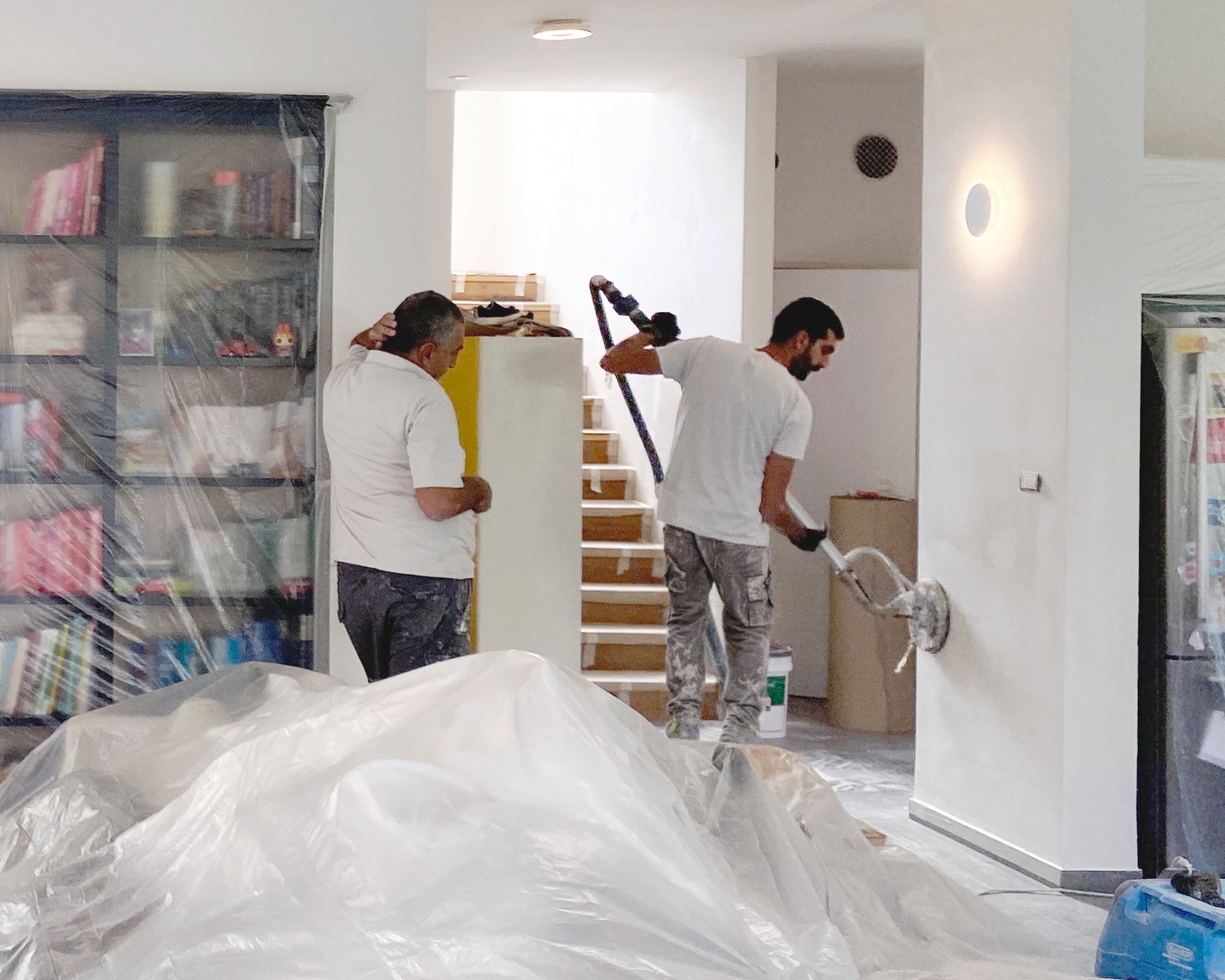 Two family painters at work inside a home, the furniture wrapped in protective sheeting
