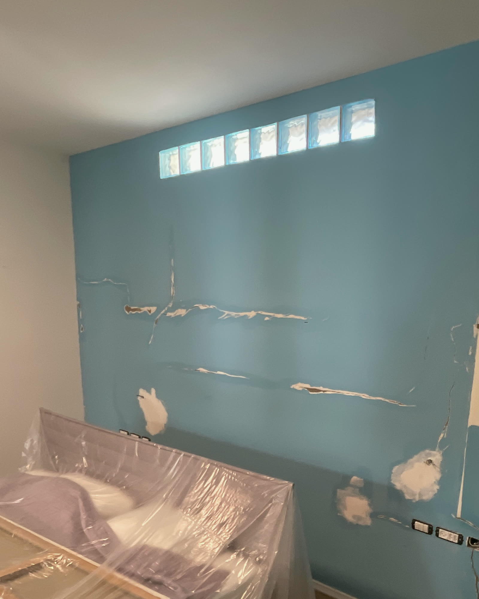 A bedroom wall mid-repair — cracks opened and filled, the furniture wrapped